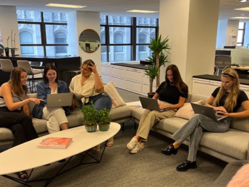 a group of women sitting on a couch with laptops